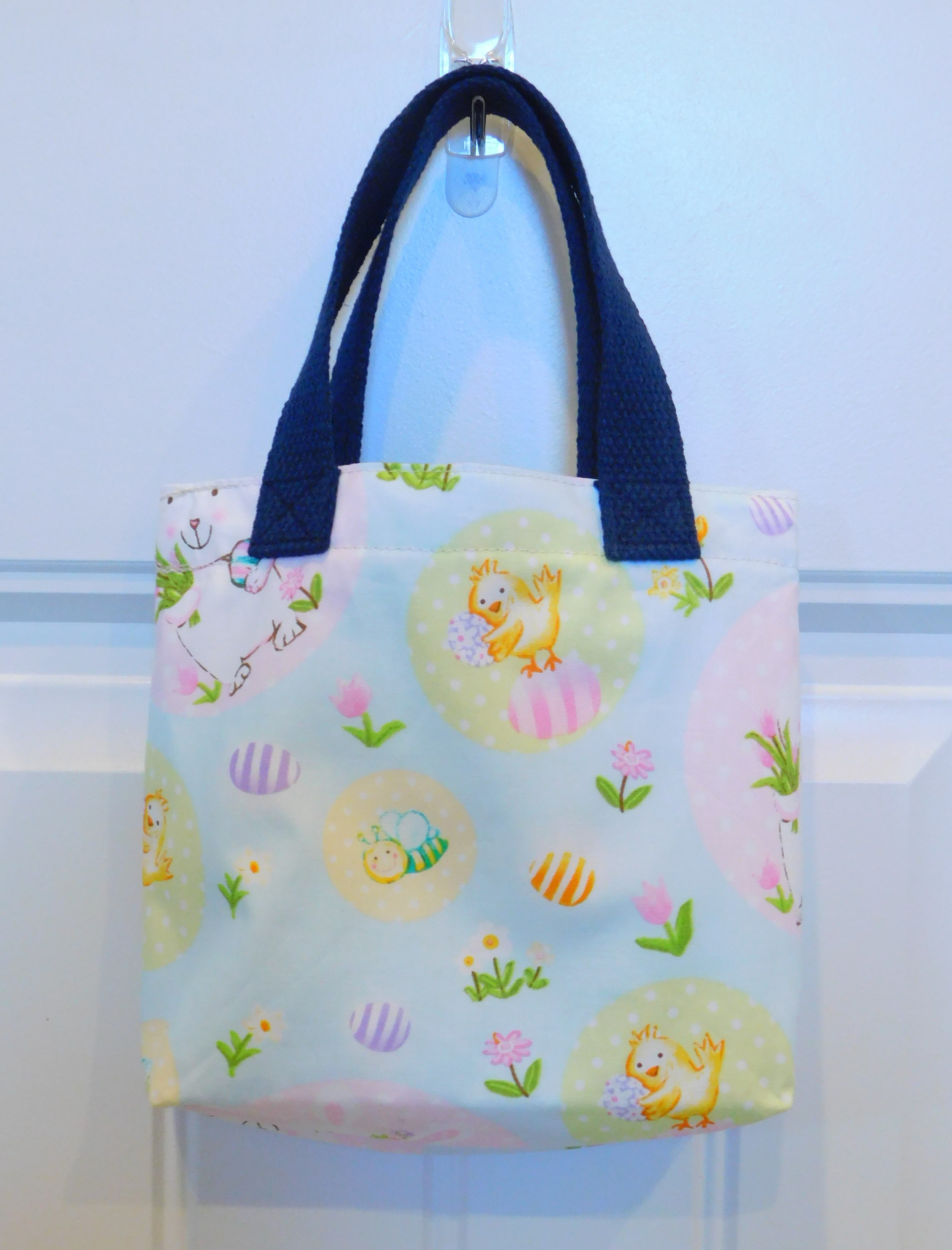 Easter bunny in a bag! This cute handmade mini tote bag is perfect for your little one to style with new Easter outfits. The mini tote has white bunnies, bees, yellow chicks, striped eggs and yellow and pink flowers. All in a background of blue and pink pastel colors. All the materials are 100% cotton. To care for your mini tote machine wash warm, tumble dry low, cool iron, non-chlorine bleach. Measurements are around 9in x 7in x 2in.