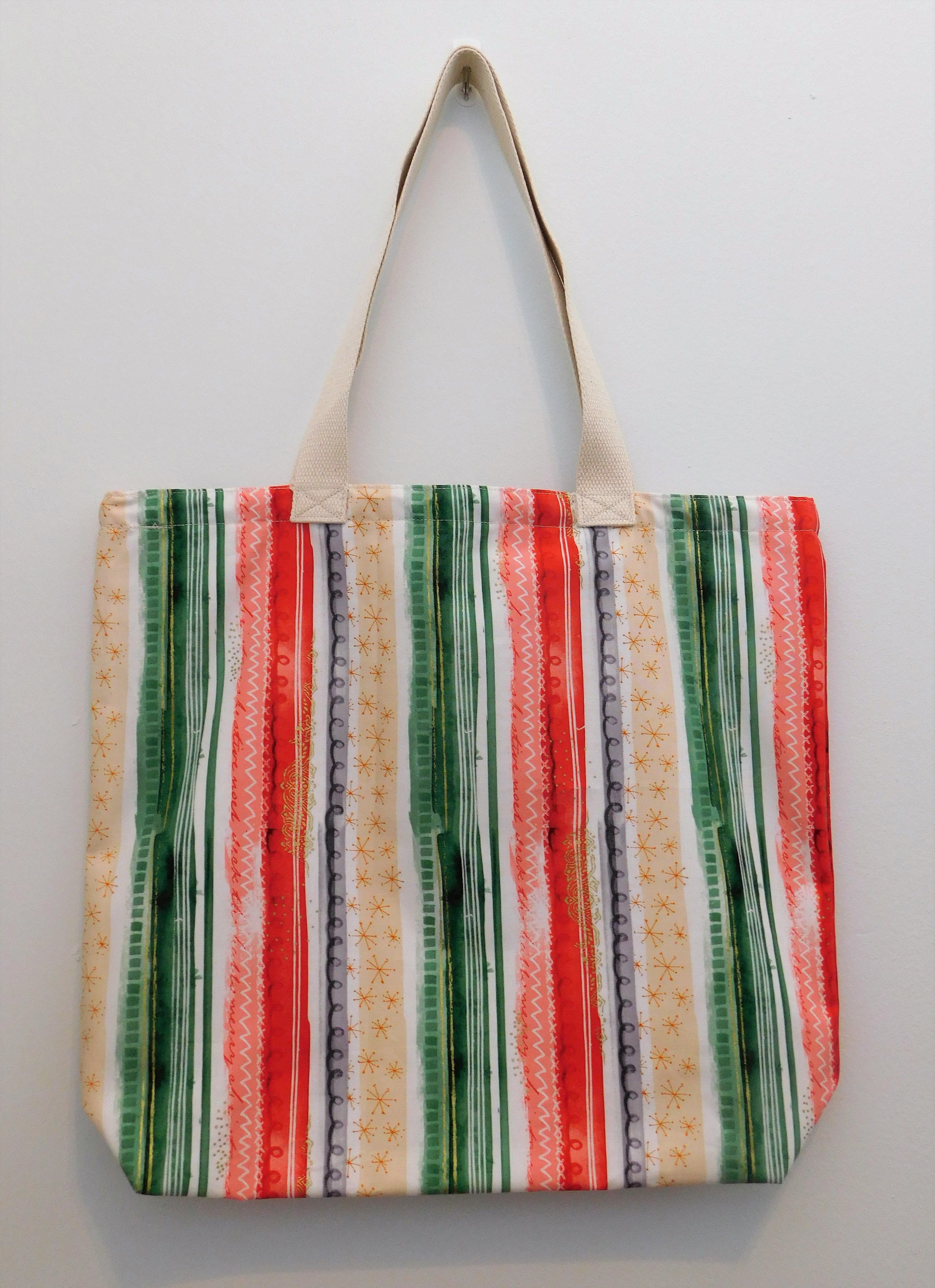 This colorful handmade tote bag is like a gift in itself! The design is like a present wrapper with light yellow, green, white, and red vertical stripes.  The fabric, muslin lining, thread and trim are 100% cotton. To care for your tote machine wash cold, tumble dry low, cool iron and no bleach. Measurements are around 16in x 19in x 4in.