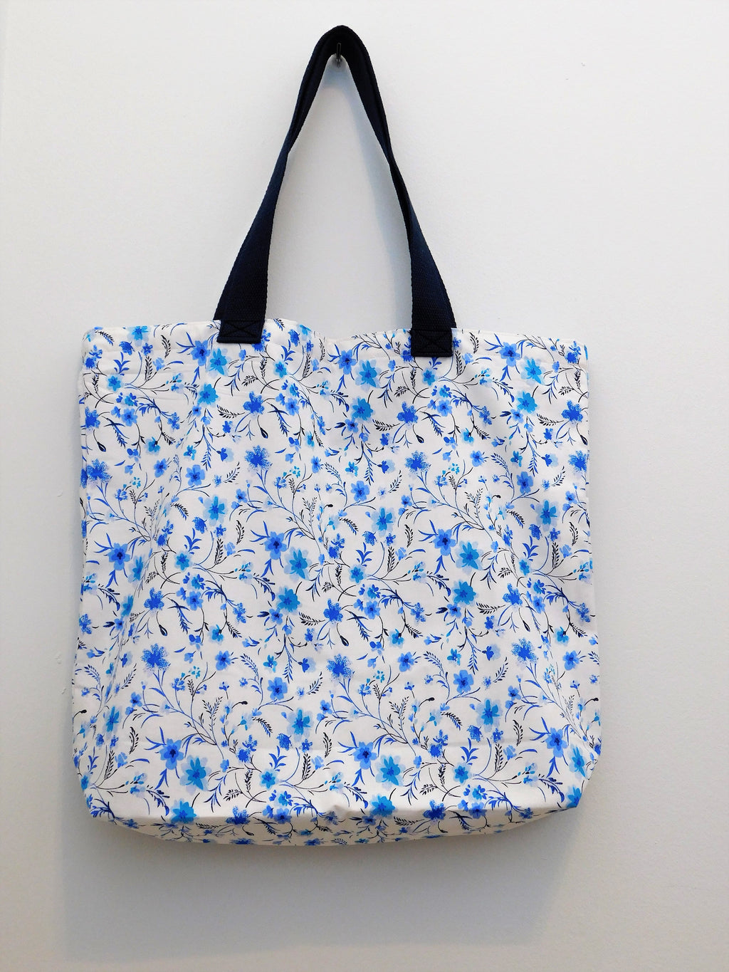 Handmade tote bag. White tote with blue flowers and navy trim. Tote is lined with white muslin fabric. Trim, tread and fabric are all 100% cotton. Measurements are around 19in x 16in x 4in.  This blue floral tote bag is perfect for spring!