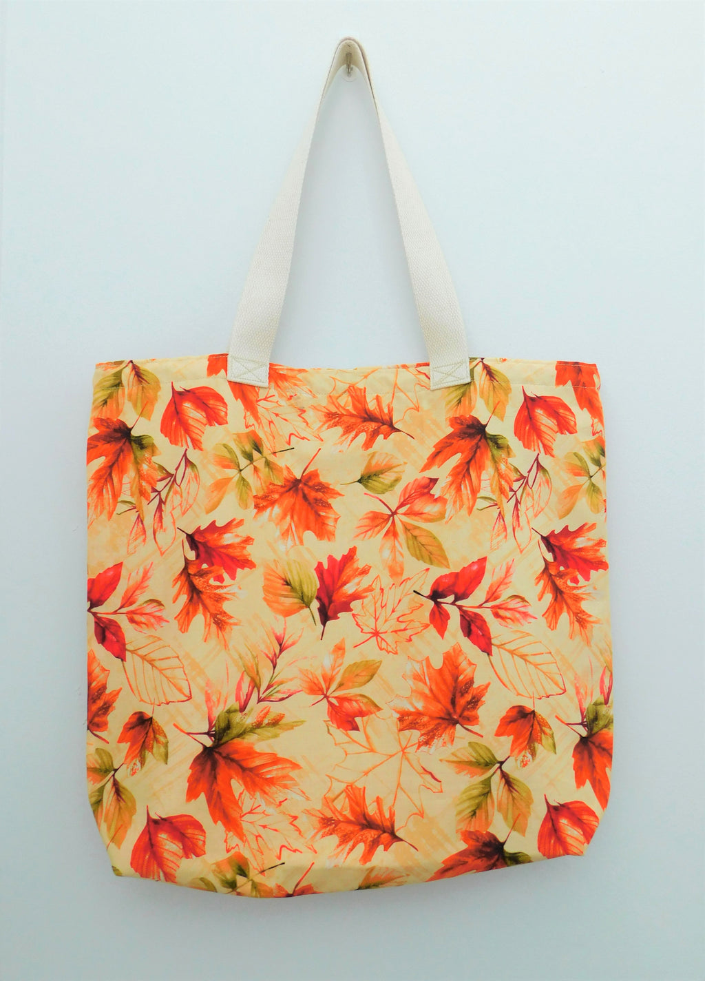 This beautiful handmade fall tote bag has different shades of orange and red leaves in a light orange colored background. Natural color trim, muslin lining, fabric, and thread are all 100% cotton. Machine wash warm, remove promptly, tumble dry low, use a cool iron, do not bleach. Measurements are around 19in x 16in x 4in.