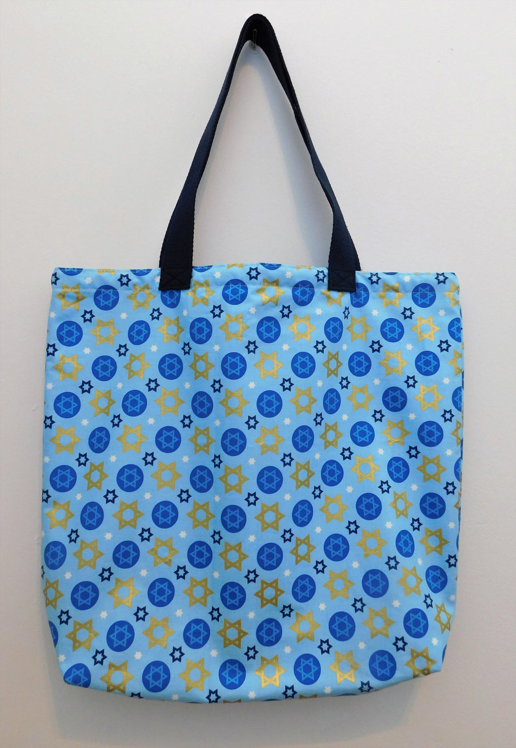 Happy Hanukkah! Light blue tote with dark blue, white and gold Stars of David. All the materials from fabric, muslin lining, thread, and trim are 100% cotton. Measurements are around 16in x 19in x 4in. To care for your tote machine wash cold, tumble dry low, do not bleach and use a cool iron.