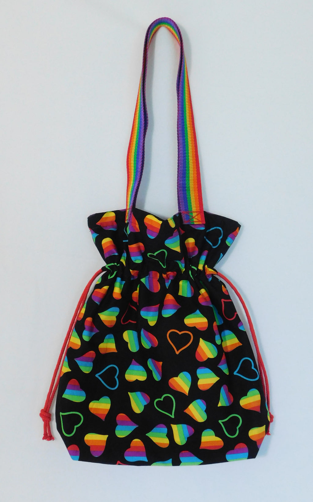 Happy Pride! This cute tote has lots of  LGBTQ+ rainbow hearts in a black background and it's just beautiful! The tote has a drawstring to secure your bag and the inside pocket is big enough to fit a cell phone and keys. Fabric, muslin lining, thread and are 100% cotton. The trim is 90% polypropylene and 10% polyester. To care for your tote machine wash gentle cold, tumble dry low, non-chlorine bleach and cool iron. Measurements are around 16in x 14 1/2in x 4in.