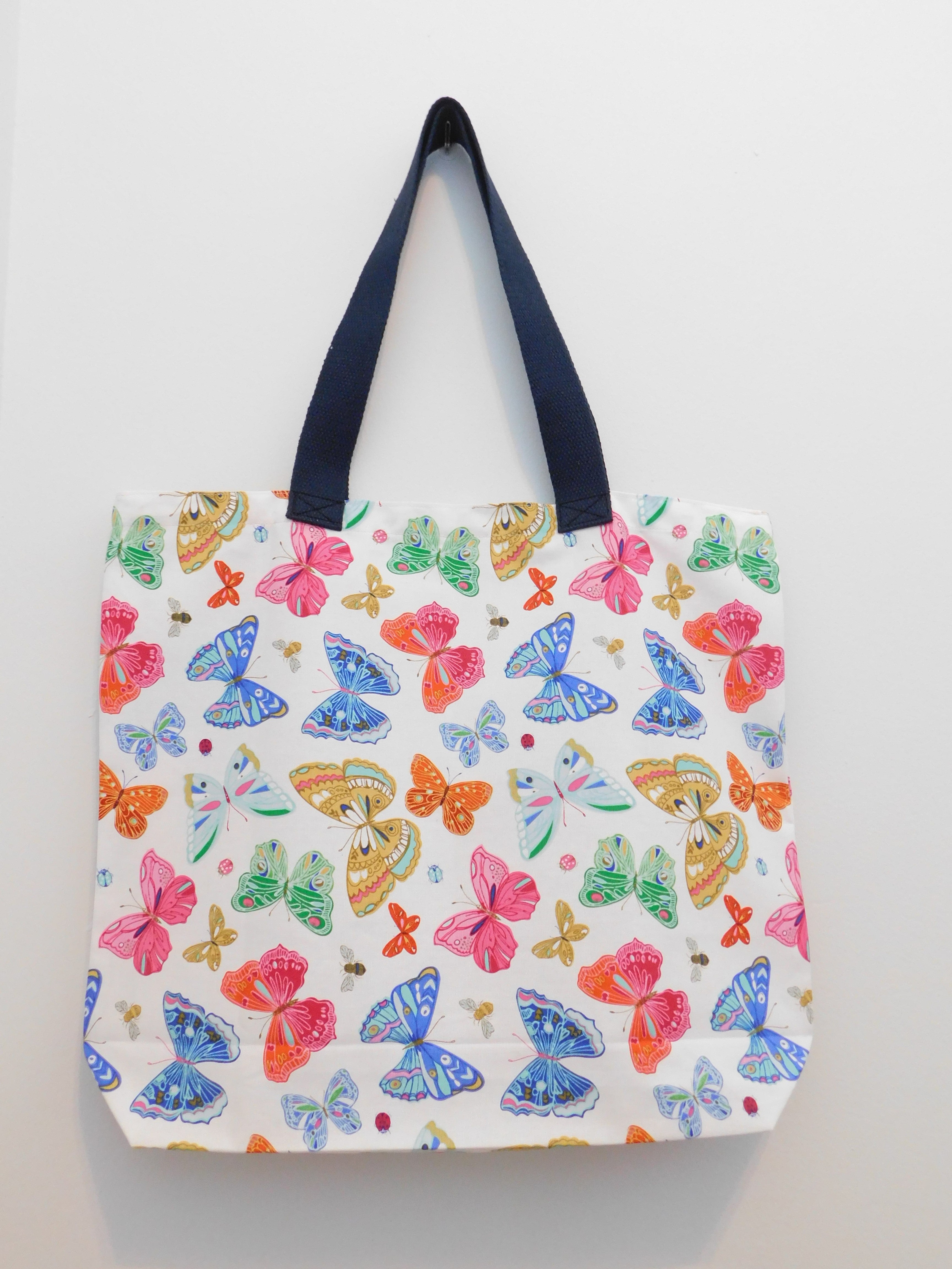 Summer is here! This hadmade tote is covered in beautiful red, blue, green, yellow, and pink butterflies and bees in a white background. The duck cloth, navy blue trim and thread are all 100% cotton.. Machine wash, remove promptly. Measurements are around 19in x 16in x 4in. 