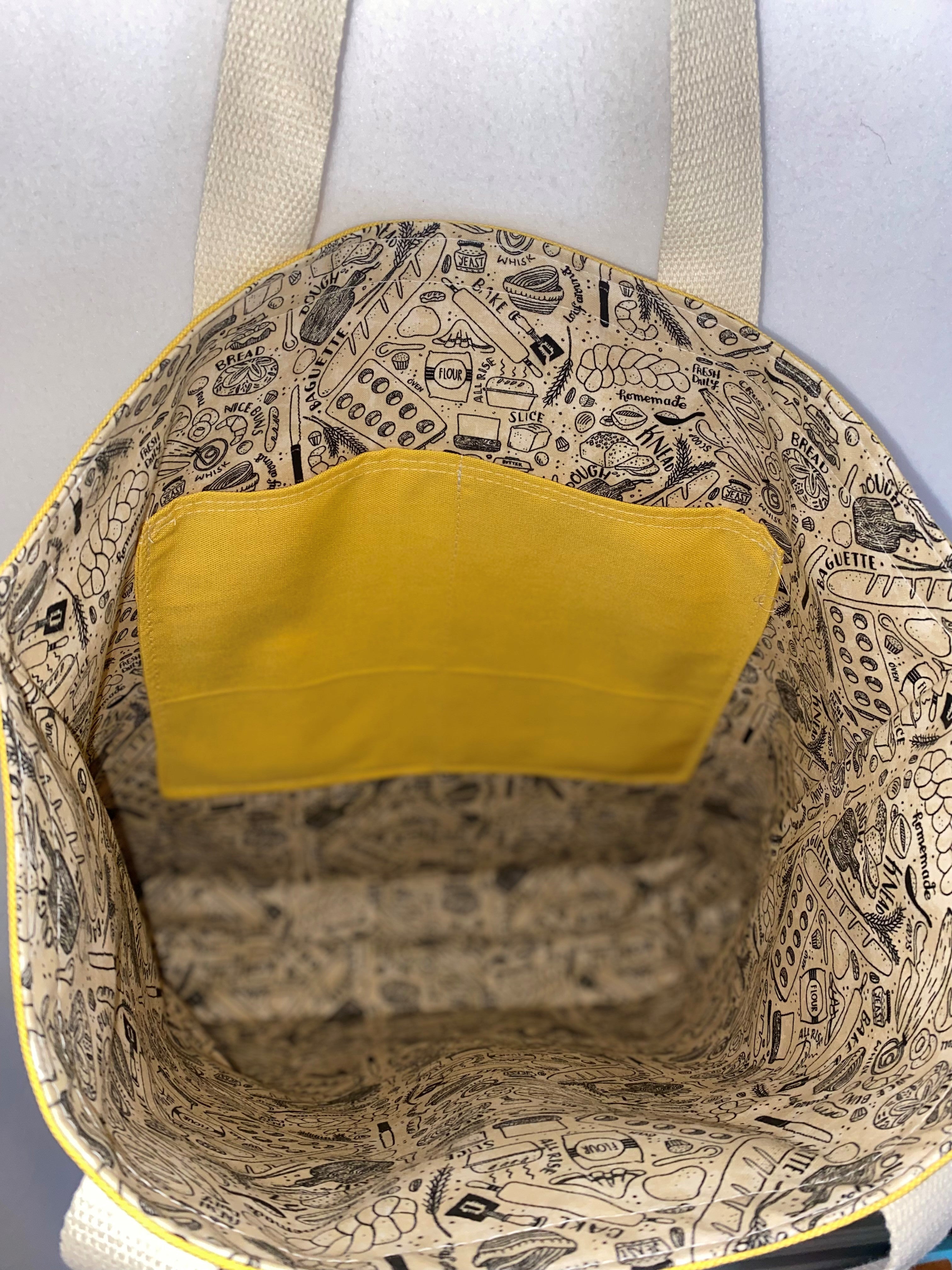 This solid mustard handmade tote bag is very spacious and really sturdy.  There is a slip pocket on the outside measuring around 8x8. The longer straps adds sturdiness to the tote. The inside is lined with a light brown fabric with bakery images such as loafs of bread and baking utensils. This tote also has a slip pocket inside big enough to fit your phone, keys and a wallet.  All the materials; fabric, lining, thread, and trim are 100% cotton.  Measurements are around 16in x 19in x 4in.