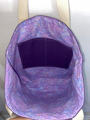 This solid purple handmade tote bag is very spacious and really sturdy.  There is a slip pocket on the outside measuring around 8x8. The longer straps adds sturdiness to the tote. The inside is lined with a light purple fabric with different specs of colors. This tote also has a slip pocket inside big enough to fit your phone, keys and a wallet.  All the materials; fabric, lining, thread, and trim are 100% cotton.  Measurements are around 16in x 19in x 4in.