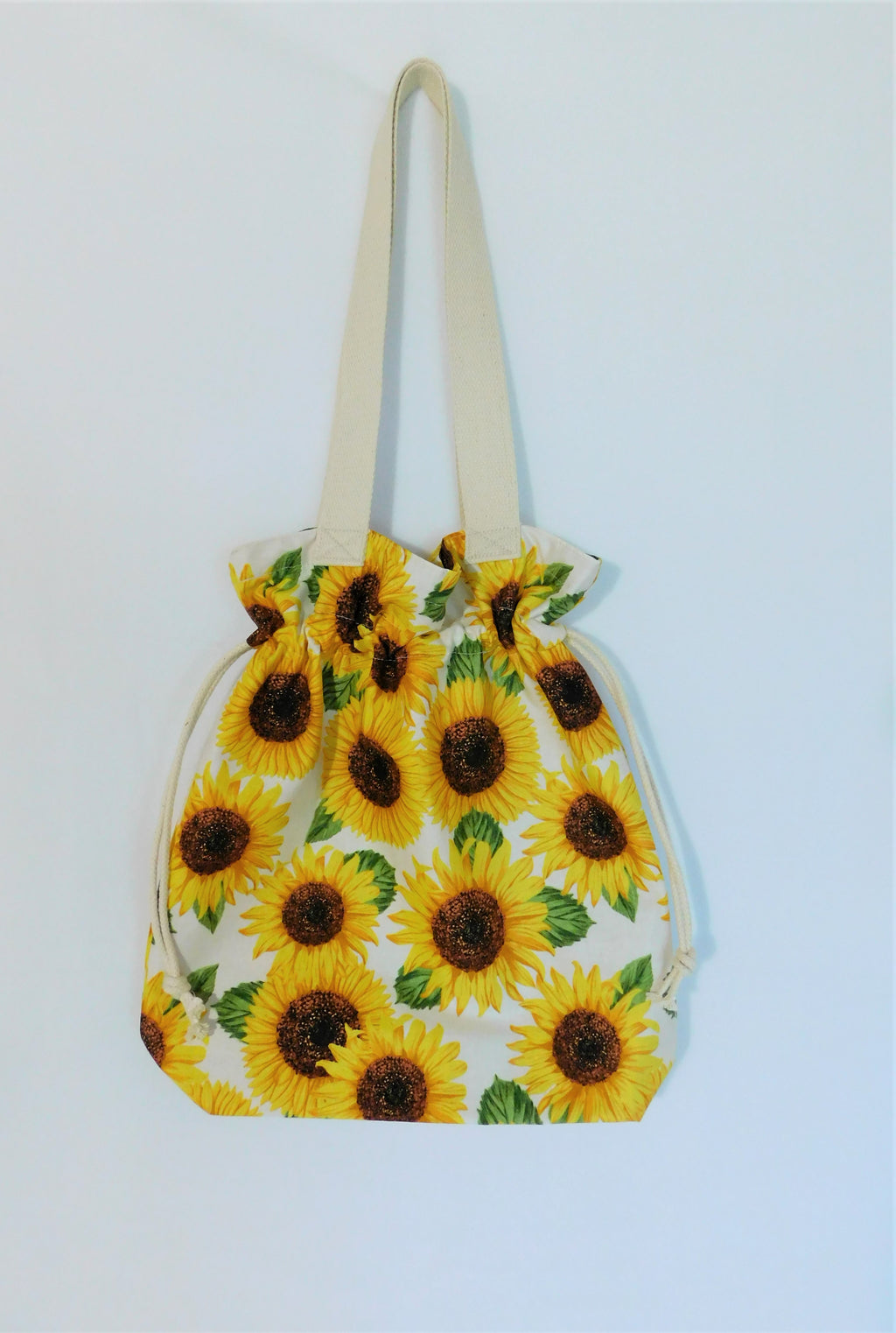 Sunflowers! This cute tote is covered in big bright yellow sunflowers in a white background and it's just too cute! It has a drawstring to secure your bag and the inside pocket is big enough to fit a cell phone and keys. Fabric, muslin lining, thread and trim are 100% cotton. To care for your tote machine wash gentle cold, tumble dry low, and cool iron. Measurements are around 16in x 14 1/2in x 4in.