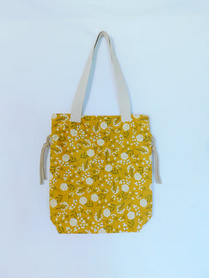 Stylish! This woodland cotton tote has white cotton flowers in a yellow mustard color background and it's just vibrant! It has a drawstring to secure your bag and the inside pocket is big enough to fit a cell phone and keys. Fabric, muslin lining, thread and trim are 100% cotton. To care for your tote machine wash gentle cold, tumble dry low, remove promptly, wash separately, do not soak or leave fabric wet in washer, dry on low heat and use cool iron. Measurements are around 16in x 14 1/2in x 4in.