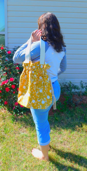 Stylish! This woodland cotton tote has white cotton flowers in a yellow mustard color background and it's just vibrant! It has a drawstring to secure your bag and the inside pocket is big enough to fit a cell phone and keys. Fabric, muslin lining, thread and trim are 100% cotton. To care for your tote machine wash gentle cold, tumble dry low, remove promptly, wash separately, do not soak or leave fabric wet in washer, dry on low heat and use cool iron. Measurements are around 16in x 14 1/2in x 4in.