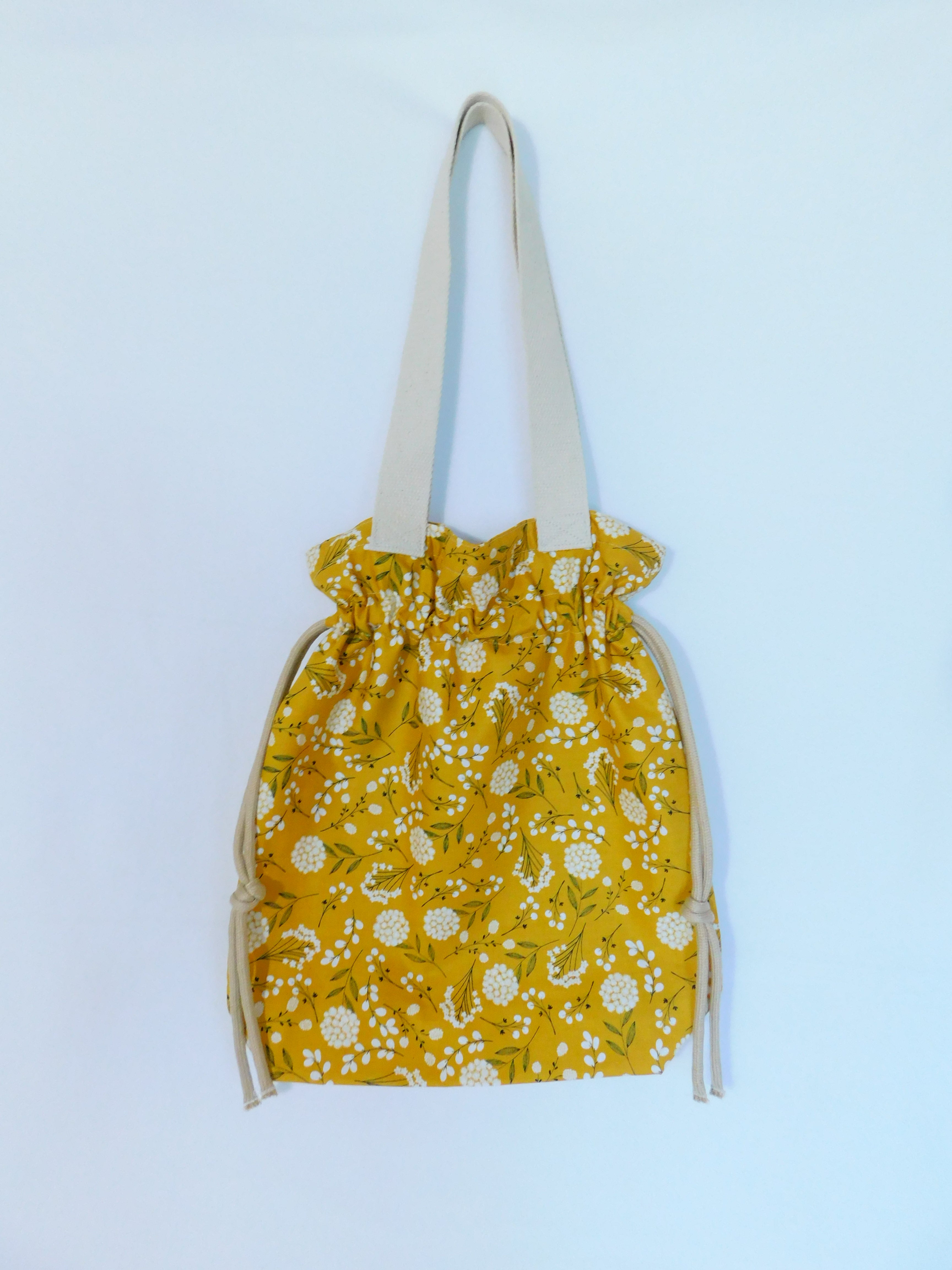 Stylish! This woodland cotton tote has white cotton flowers in a yellow mustard color background and it's just vibrant! It has a drawstring to secure your bag and the inside pocket is big enough to fit a cell phone and keys. Fabric, muslin lining, thread and trim are 100% cotton. To care for your tote machine wash gentle cold, tumble dry low, remove promptly, wash separately, do not soak or leave fabric wet in washer, dry on low heat and use cool iron. Measurements are around 16in x 14 1/2in x 4in.