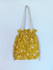 Stylish! This woodland cotton tote has white cotton flowers in a yellow mustard color background and it's just vibrant! It has a drawstring to secure your bag and the inside pocket is big enough to fit a cell phone and keys. Fabric, muslin lining, thread and trim are 100% cotton. To care for your tote machine wash gentle cold, tumble dry low, remove promptly, wash separately, do not soak or leave fabric wet in washer, dry on low heat and use cool iron. Measurements are around 16in x 14 1/2in x 4in.